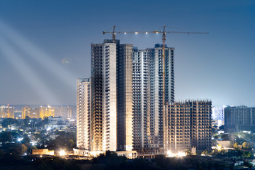 aerial shot of under construction buildings with two beams of light coming from them at night lit from the base with a crane at the top