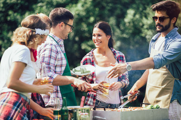 Barbecue party. Group of people standing around grill, chatting, drinking and eating.
