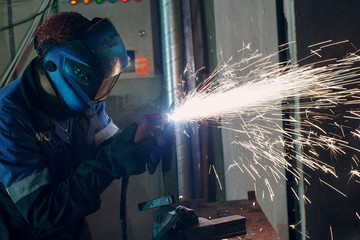 Man in mask cuts metal with plasma cutter. Helmet and spakrs.
