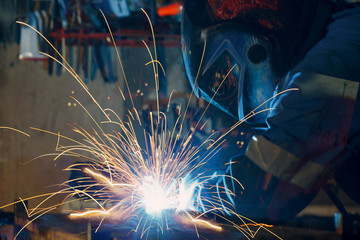 Welder welding metal construction on factory.