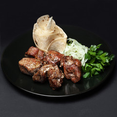 hot skewers on a black plate with pita bread and herbs on a black background.