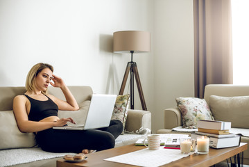 Young blonde woman on sofa woking remotely from home.