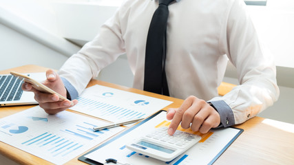 Business man are pressing the calculator to calculate the budget with business graph in the office.