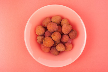 several lychee fruits lie on a coral plate on a pink background