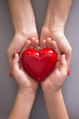 Mother care or love concept with child and mom hands holding a red heart shape