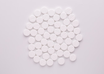 A lot of medical pills on a white table surface. A pile of round white pills.