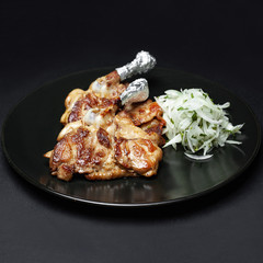 grilled chicken leg on the bone on a black plate on a black background.