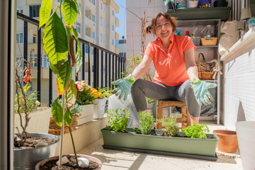 Quarantine Stay at Home concept: A happy and smiling woman is showing her cultivated vegetables in a pot at her city balcony.