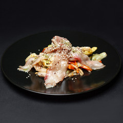 vegetable salad with fish on a black plate on a black background.