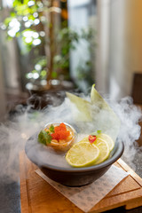Scallop with caviar and lemon in asian style with smoke on summer terrace bokeh