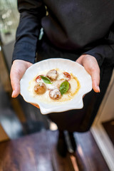 Scallop with tomatoes and sauce and basil in waiter hand on terrace cafe bokeh