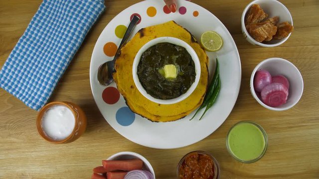 Woman hands placing a thali of Punjabi cuisine - Sarson ka saag and Makki ki Roti. Closeup shot of Punjabi food Makki ki Roti and Saag served with Kulahad Lassi  salad  pickle  mint chutney  and ja...