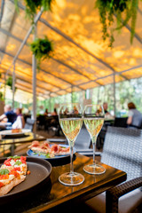 Two glasses of white wine with bruschetts on summer terrace bokeh sunlight leaf cafe