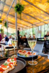 Two glasses of white wine with bruschetts on summer terrace bokeh sunlight leaf cafe