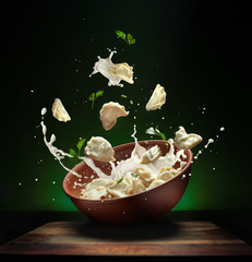 Hot pierogi flying out of the clay bowl with cream and parsley. Some vareniki stay inside the...