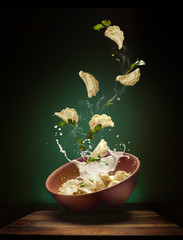 Hot pierogi flying out of the clay bowl with cream and parsley. Some vareniki stay inside the...