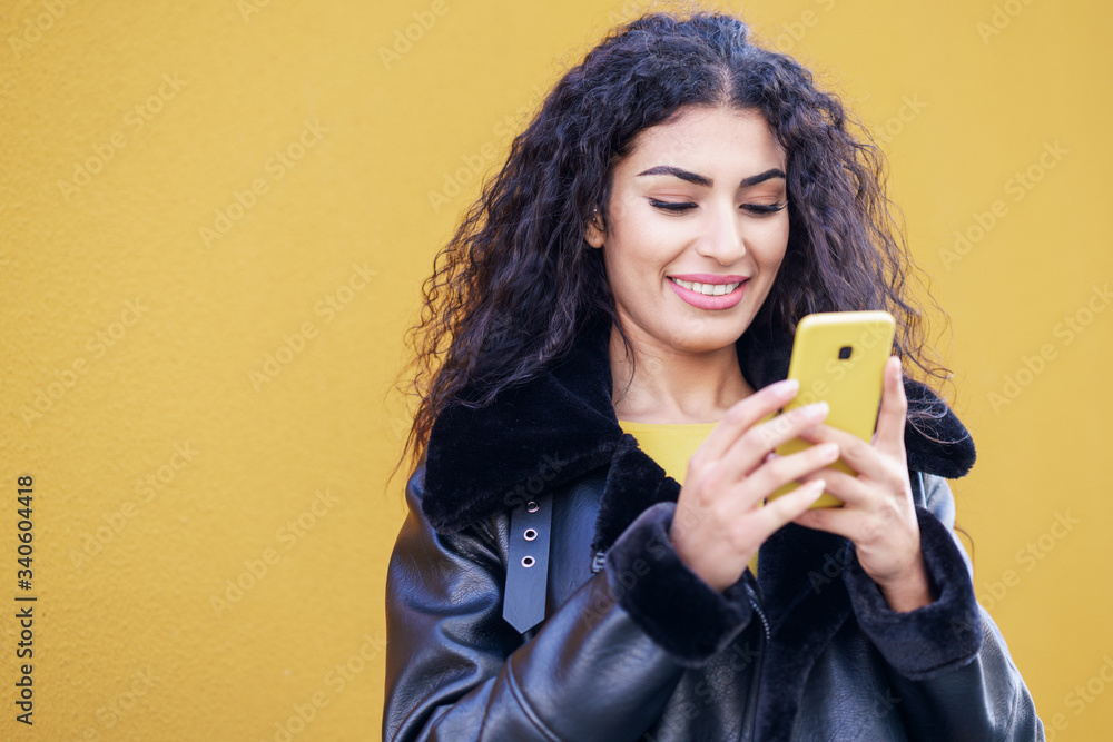 Wall mural young arab woman walking in the street using her smartphone