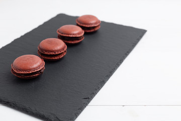 Obraz na płótnie Canvas delicious chocolate macarons on Slate plate on white wooden background