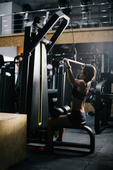 Sporty young woman with perfect athletic body wearing black sportswear using training simulator for...