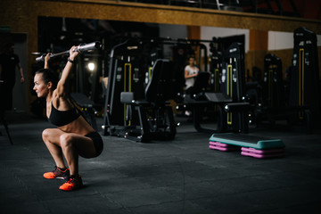 Fototapeta na wymiar Strong young woman with perfect athletic body wearing black sportswear lifting empty vulture from the barbell overhead during sport workout training in modern dark gym. Concept of healthy lifestyle.