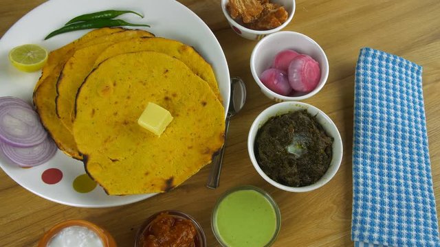 Closeup shot - Punjabi Thali with Makii Ki roti and butter revolving on a turntable. High angle shot of north Indian food Makki Ki Roti and Sarson ka saag served with Lassi  salad  pickle  mint chu...
