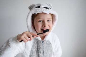 the little girl woke up in the morning and brushes her teeth with black coal toothpaste. The girl is wearing pajamas in the animal