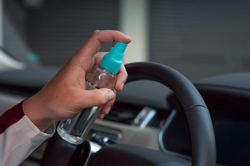 Hand of woman is spraying alcohol,disinfectant spray on steering wheel in her car,prevent infection of Covid-19 virus,contamination of germs or bacteria,wipe clean surfaces that are frequently touched