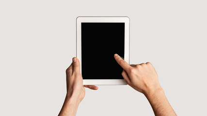 Young man touching blank screen of tablet computer on light background, close up. Mockup for design. Panorama