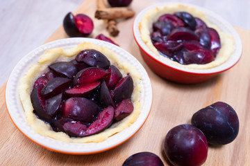 Traditional German glazed plum tartelettes in miniature pie dishes with cinnamon sticks