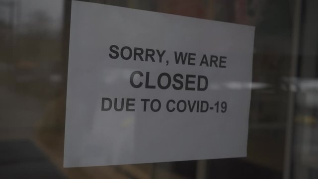 A shop owner puts a SORRY, WE ARE CLOSED DUE TO COVID-19 sign on the front door. Take out or carry away quickly became the only option for restaurants and bars during the coronavirus pandemic of 2020.