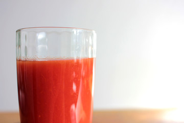 Glass of tomato juice on table on blurred background in kitchen interior. Natural lighting
