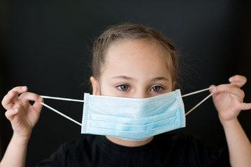 European young girl puts on a medical mask. Conceptual photo on the theme of the covid-2019 pandemic. Isolated on a black background.