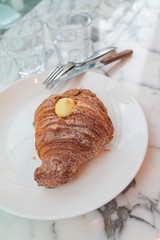 Croissant bread with butter with fork and knife on a white marble stone texture table.