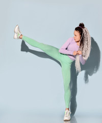 Young beautiful girl with modern hairstyle in sportswear standing and making kick by leg