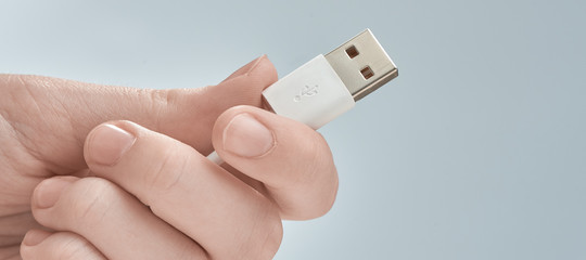 Hand holding white USB cable isolated on gray background.