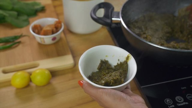 Indian female serving delicious Punjabi cuisine Sarson ka saag in a white bowl. Closeup shot of woman hands pouring freshly cooked saag in a ceramic bowl with a cooking spoon - winters food concept