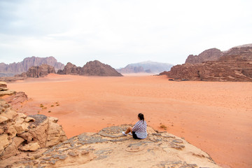 Girl sitting on a rock. Sand-dunes and rocks in Wadi-Rum desert, Jordan, Middle East