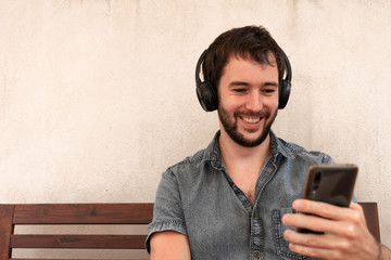 Handsome boy with bluetooth headphones looking at his mobile phone, while smiling positively