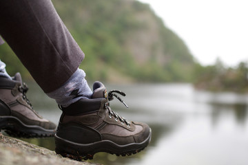 Naklejka premium person sitting with hiking shoes by water