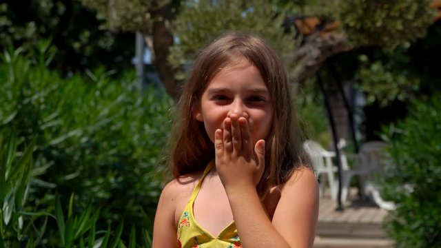 Adorable cute taned girl with big brown eyes is waving her hand and blowing a kiss outdoors