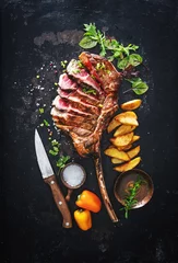 Schilderijen op glas Grilled meat, sliced ​​tomahawk beef steak with spices, french fries and vegetables © Alexander Raths