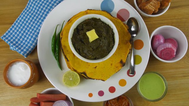 Closeup shot of woman hands adding butter to traditional Punjabi cuisine - Saag. Top view - Punjabi thali with Makki Ki Roti and Sarson ka saag served with Lassi  salad  pickle  mint chutney  and j...