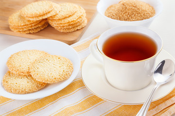 A white cup of black tea with sesame cookies on the table served at sunny morning