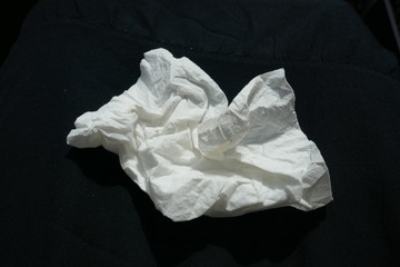 Paper handkerchief, use and throw away.  Close up, crumpled up,  isolated on black background. Use...