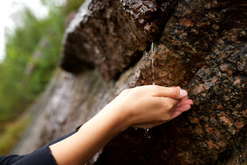 Close up young woman hands reaching for water dripping from rock