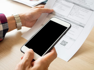 Close up hand holding smart phone to scan QR code from invoice on papers for the bills. Online bill payment concept