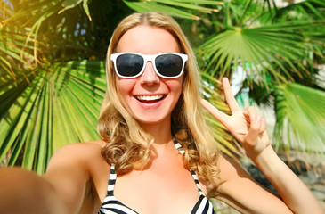 Portrait of happy smiling woman stretching hand for taking selfie over palm tree background