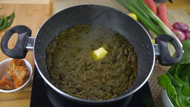 Pan shot of healthy and freshly prepared Sarson ka saag - Indian Punjabi cuisine. Closeup shot of traditional Punjabi food saag being cooked on an induction cooker surrounded with vegetables on a k...