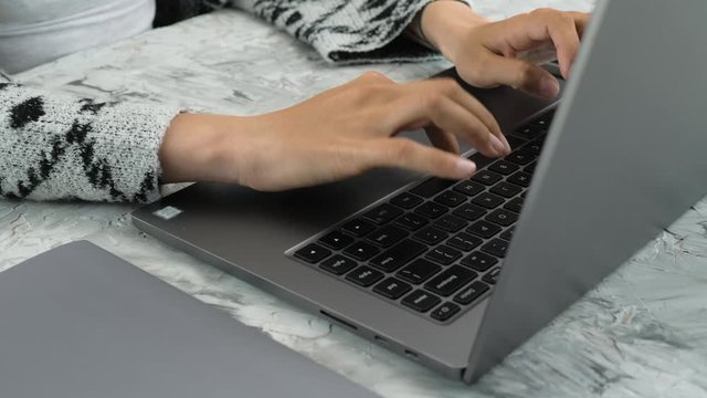 Young caucasian woman's hands typing on the keyboard of laptop, real time video, grey color spectrum, grey background, natural light, office working, freelance, actual lifestyle