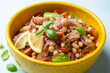 Healthy salad with tuna, white beans, cherry tomatoes, red onion and basil leaves in ceramic bowl on concrete background
